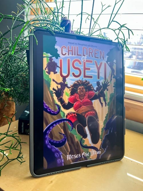 Children of Useyi by Moses Ose Utomi (Book 2) is displayed on an iPad leaning against a black planter