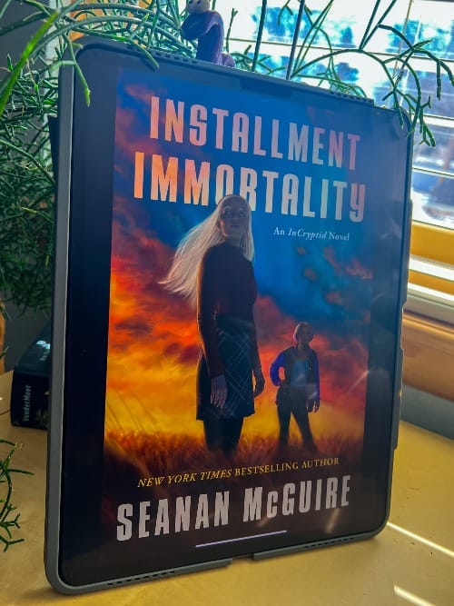 Installment Immortality - An InCryptid Novel by Seanan McGuire is displayed on an iPad leaning against a black planter