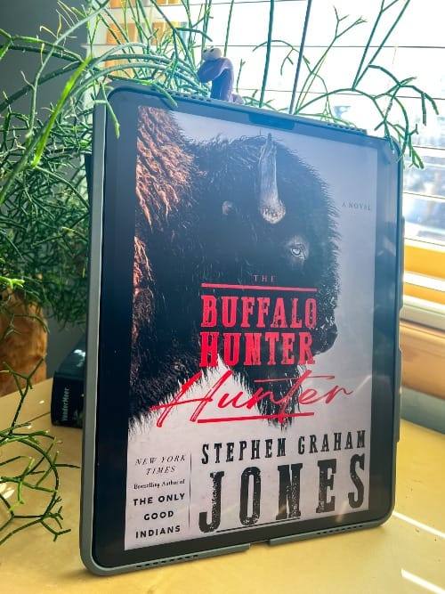 The Buffalo Hunter Hunter by Stephen Graham Jones is displayed on an iPad leaning against a black planter