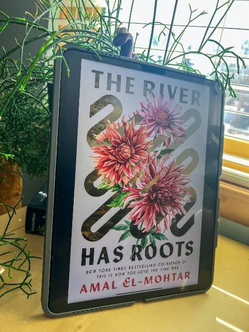 The River Has Roots by Amal El-Mohtar is displayed on an iPad leaning against a black planter