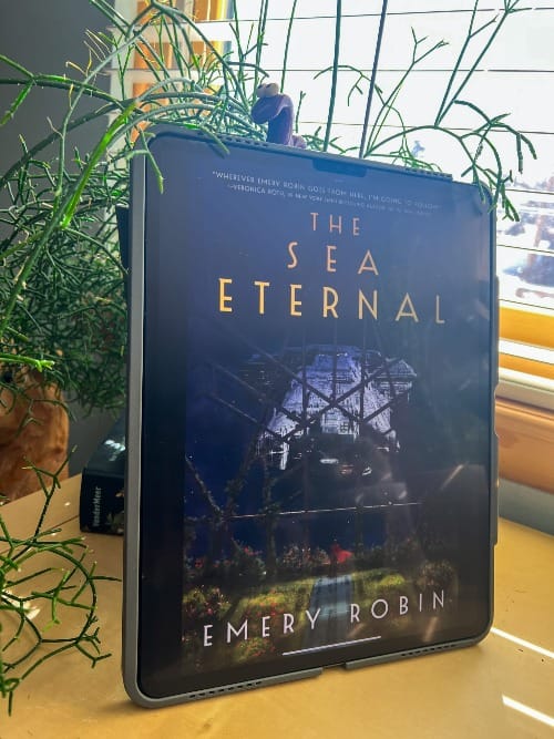 The Sea Eternal by Emery Robin (Book 2) is displayed on an iPad leaning against a black planter